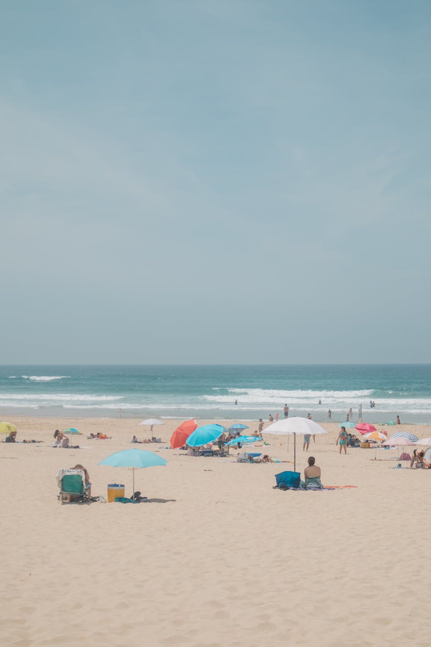 A vibrant beach scene with people relaxing under colorful umbrellas on a sunny day.