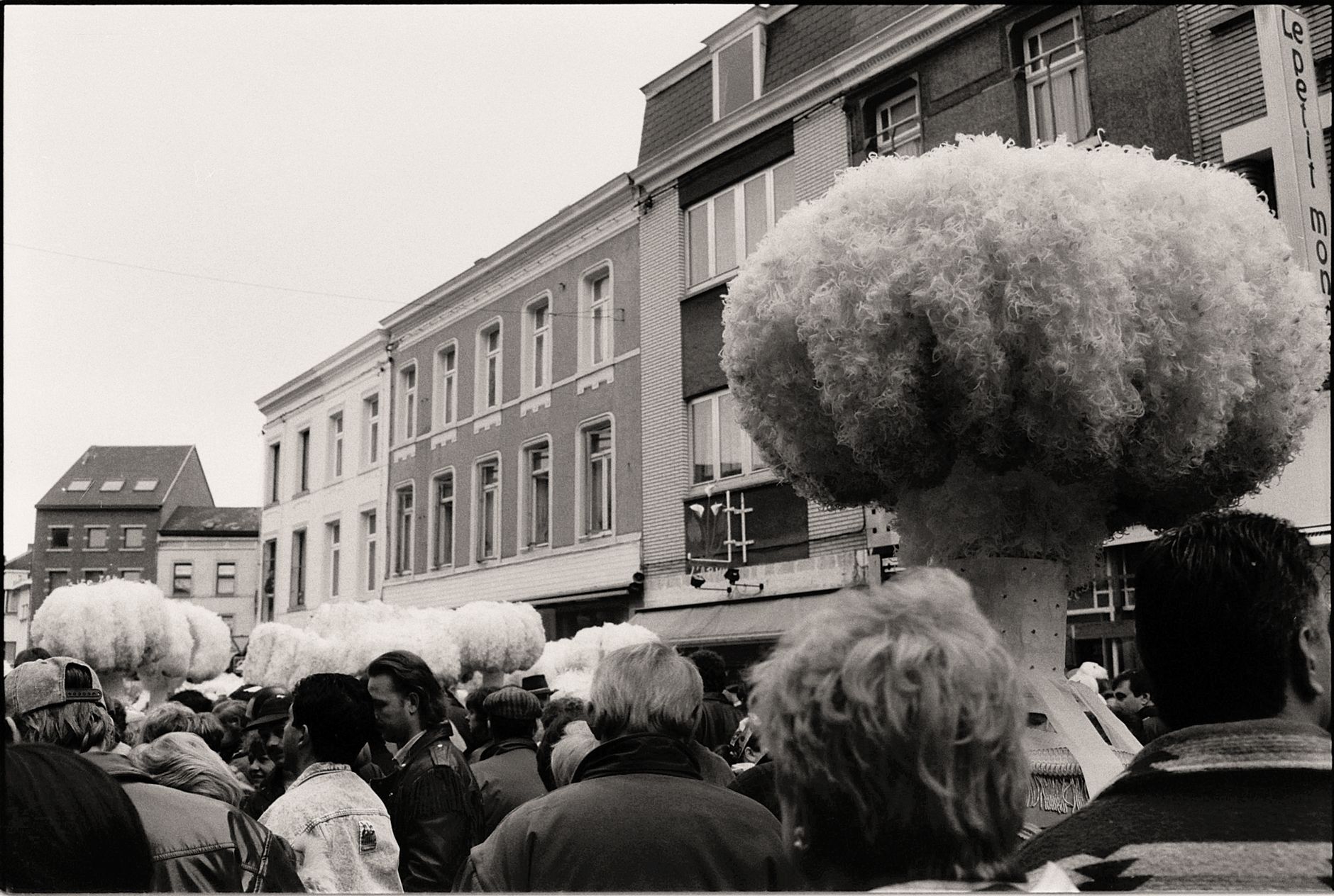 Black and white photo of a festive parade with people wearing large fluffy hats.