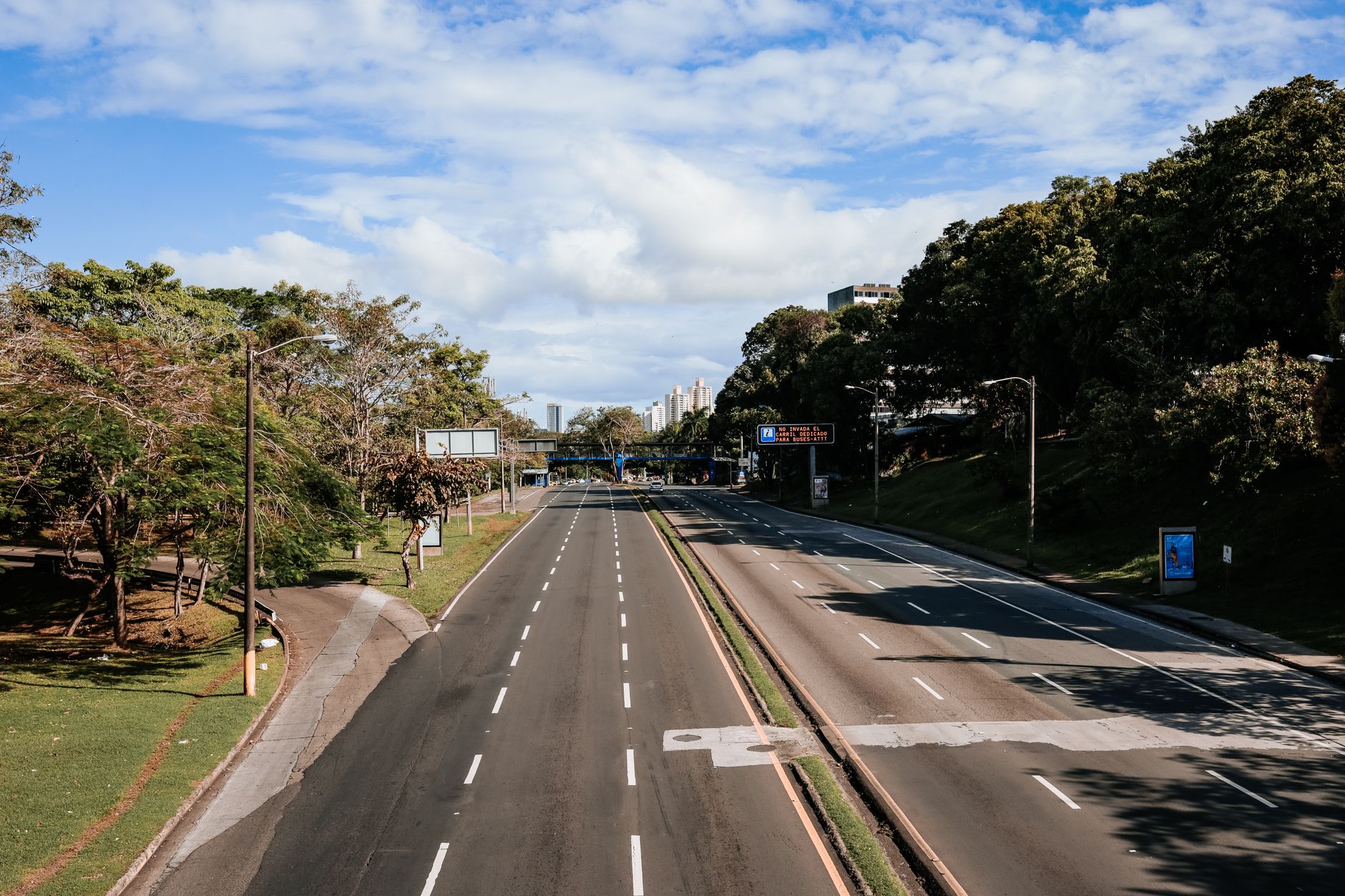 An empty highway lined with greenery, captured in clear daylight under blue skies.