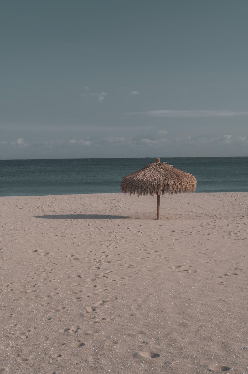 Calm beach scene featuring a solitary straw umbrella on a sandy shoreline, ideal for summer relaxation.