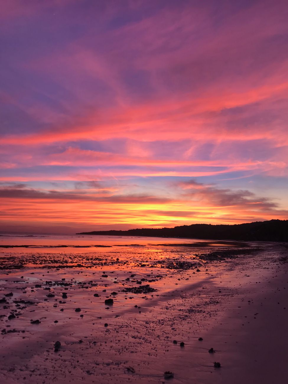 Vibrant sunset over a tranquil beach in Indonesia, with hues of pink and orange reflecting on the water.