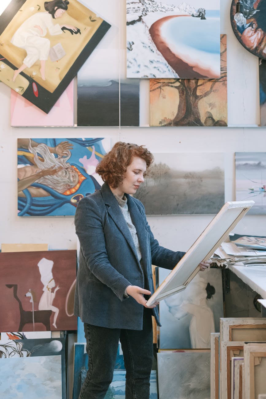 A woman in a blazer reviews a canvas in an art gallery filled with paintings. Artistic atmosphere.