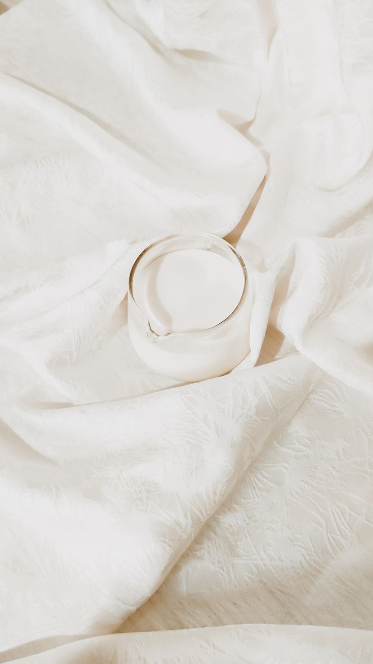 A delicate minimalist shot of a glass of milk on textured white fabric, highlighting simplicity.