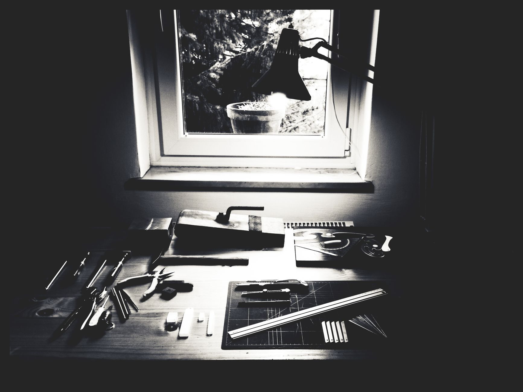 Monochrome workbench setup with crafting tools and equipment near a window.