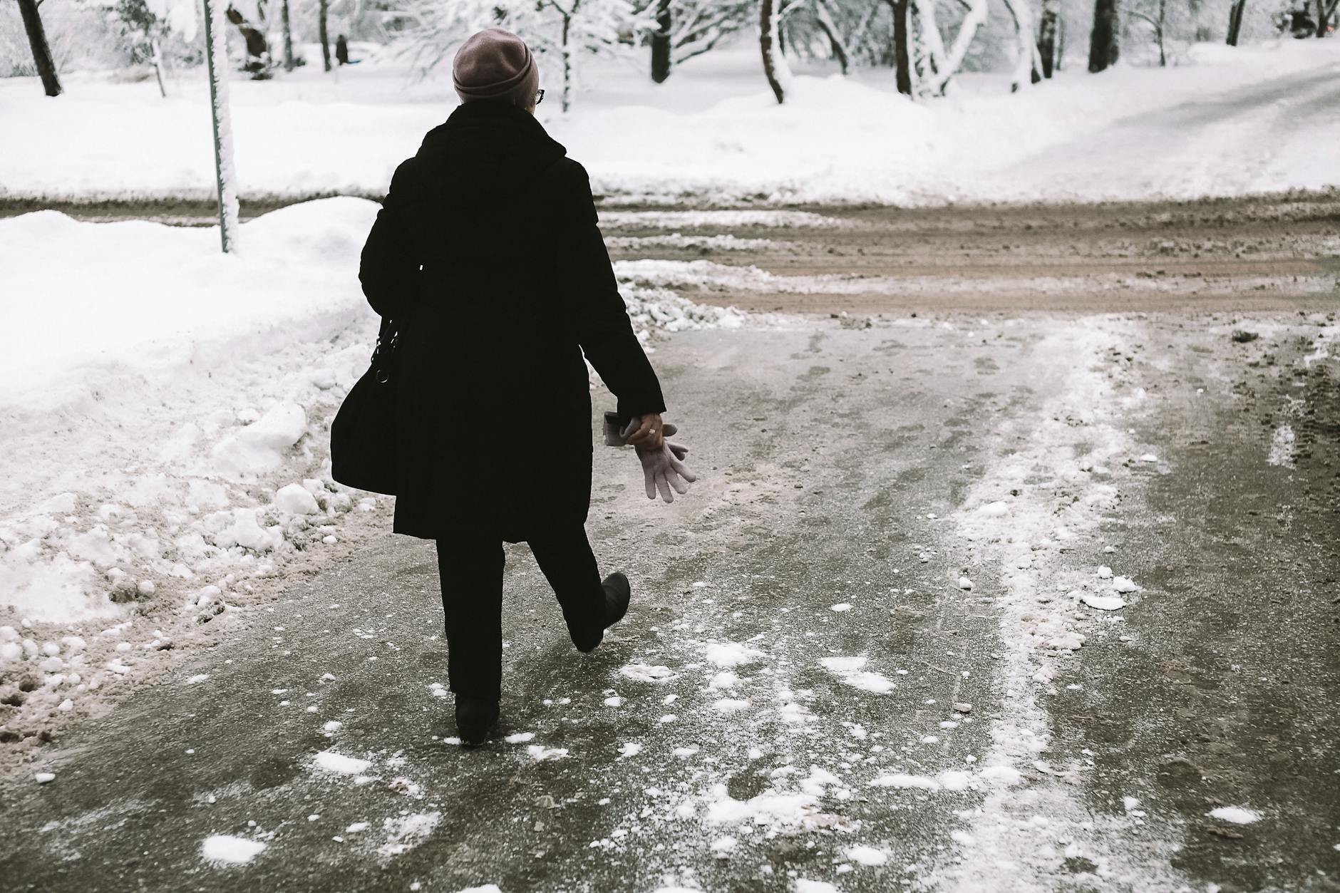 A person in a trench coat walks on a snowy road, embracing the winter weather.