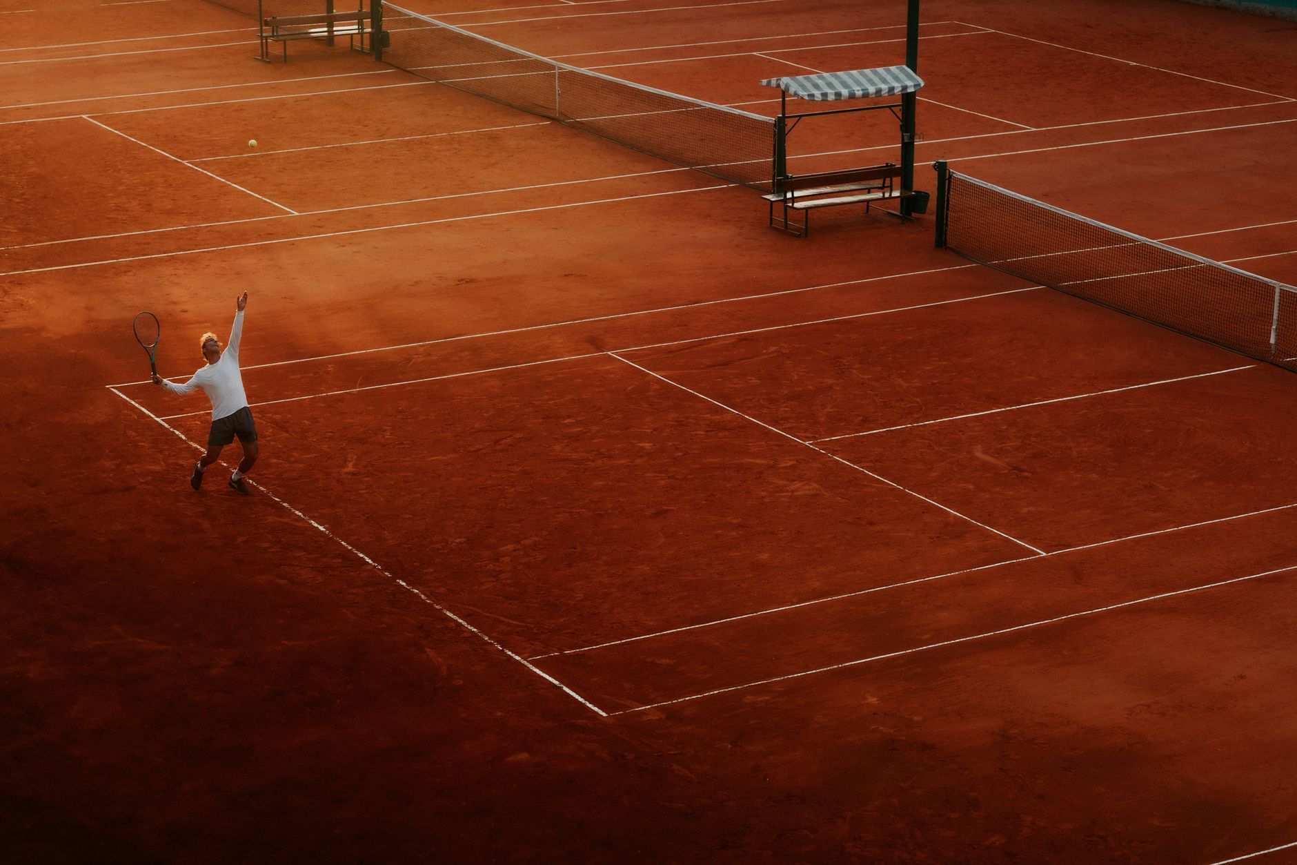A player serves on a clay tennis court, highlighting the beauty and intensity of the sport at sunset.