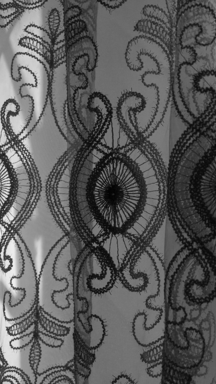 Detailed black lace curtain pattern illuminated by soft indoor light