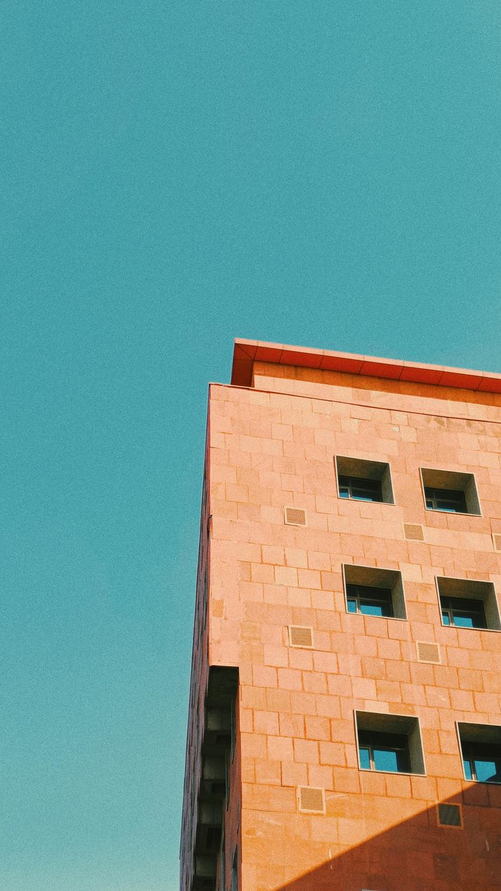 A modern, geometric building shot from below against a clear, blue sky.