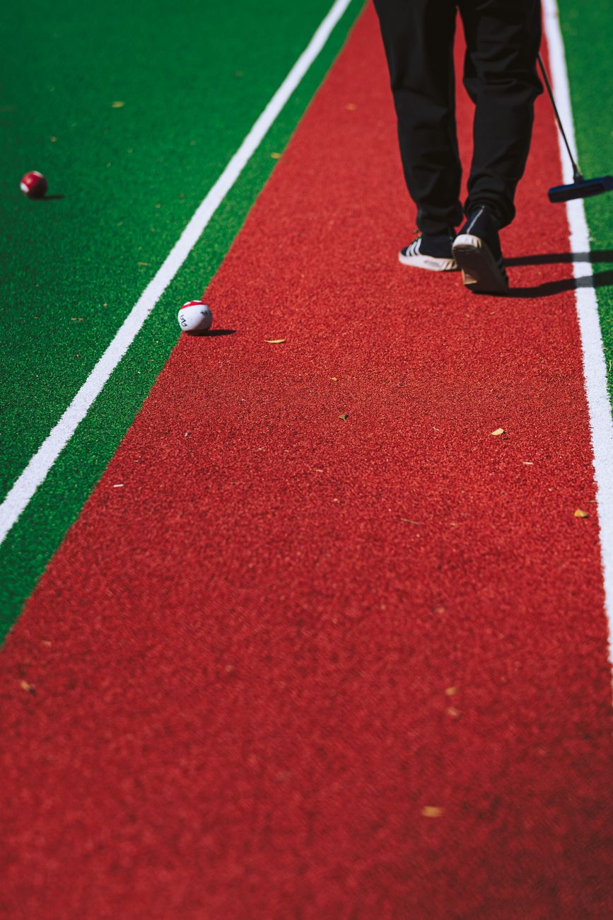 Player walking on vibrant gateball field with balls scattered around.