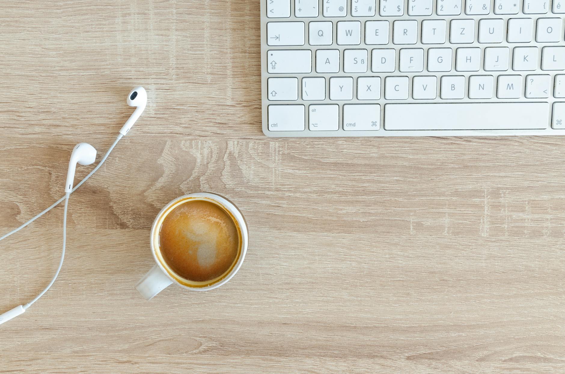 A minimalist desk featuring a keyboard, coffee cup, and earphones on a wooden surface.