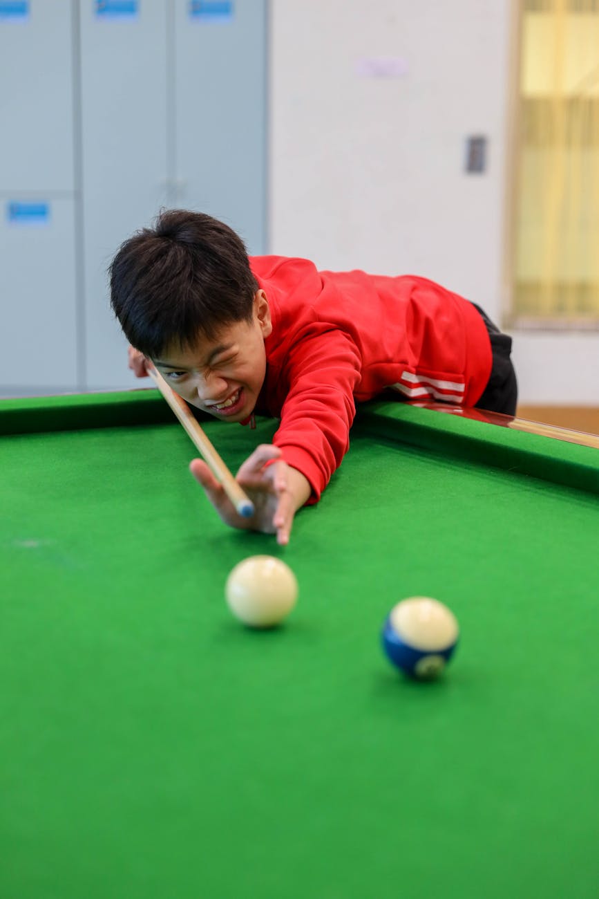 Teen boy focusing on shot in billiard game, indoor setting.