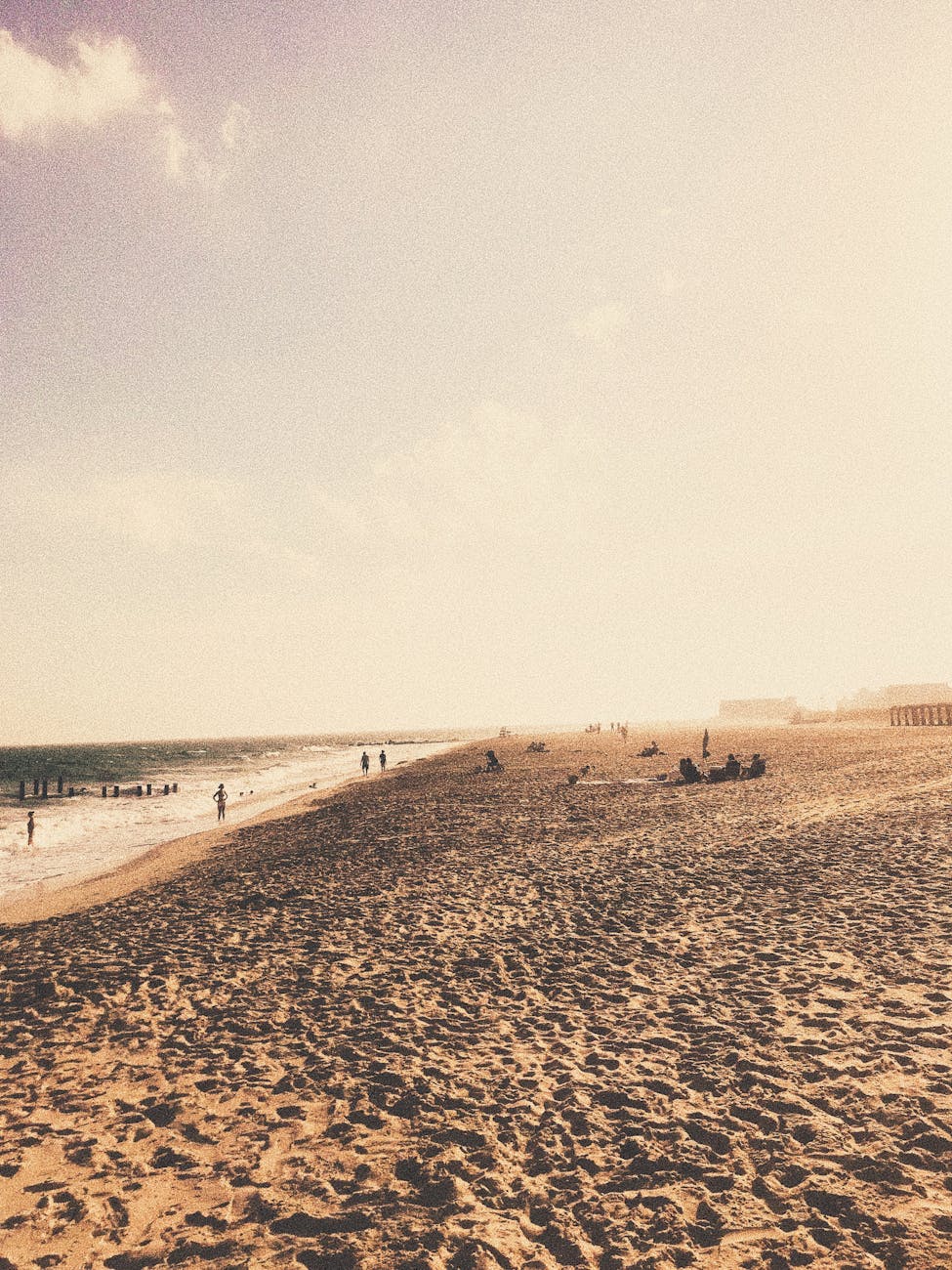 Long sandy beach with footsteps and people enjoying foaming sea in sunny day
