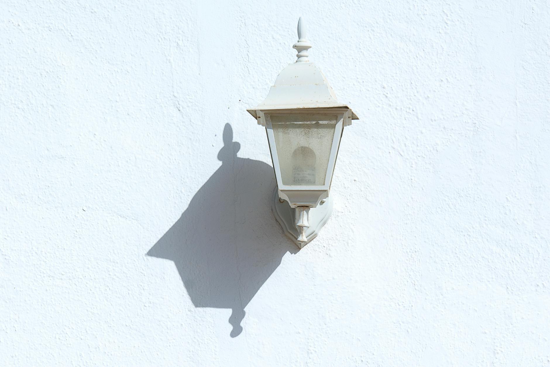 A classic decorative outdoor wall lamp casting a sharp shadow on a white textured wall.
