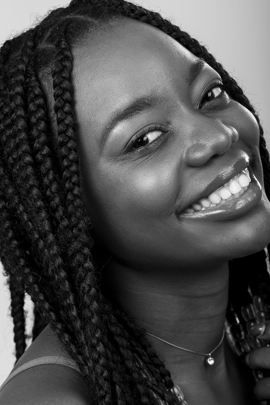 Black and white portrait of a smiling woman with braided hair in a studio setting.