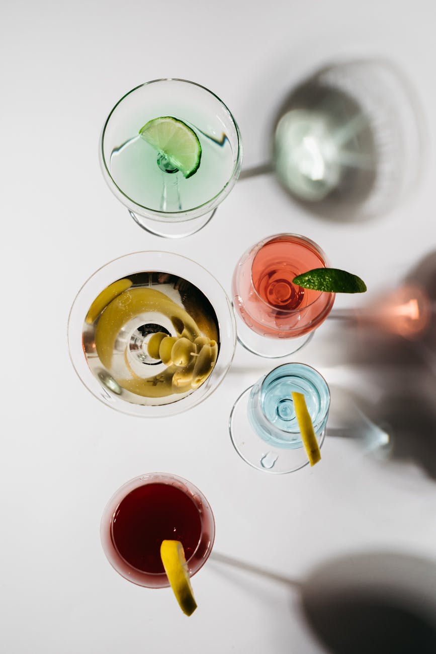 A vibrant assortment of cocktails viewed from above cast shadows on a white surface.