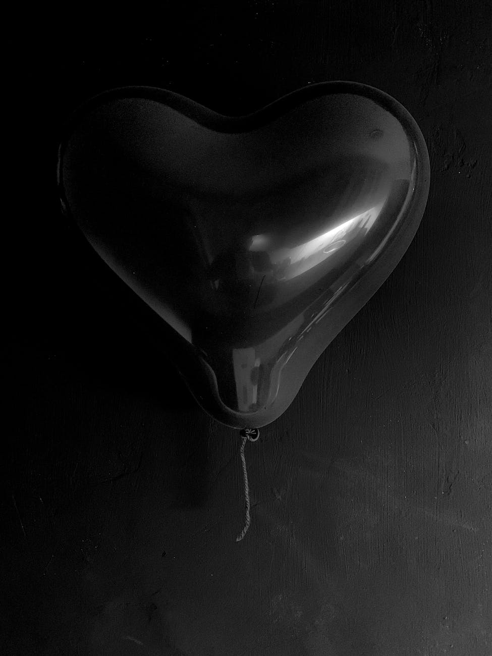 A monochrome image of a black heart-shaped balloon against a dark background.
