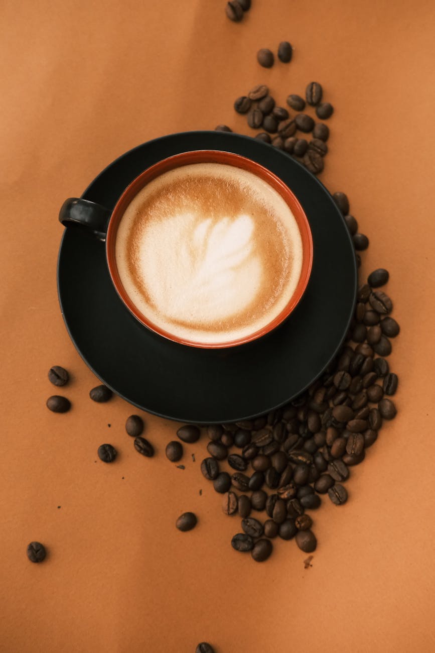 A beautifully crafted latte with coffee art surrounded by coffee beans on a rich brown background.
