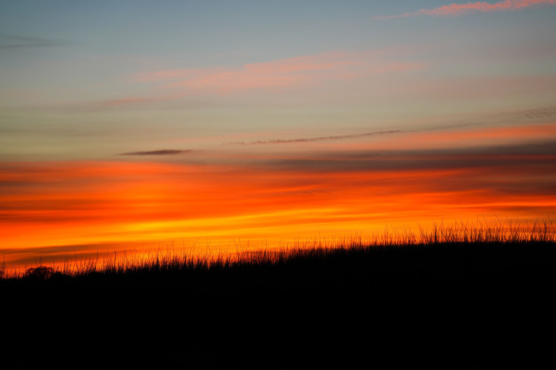 A vibrant sunset with fiery orange and red hues over a silhouetted landscape.