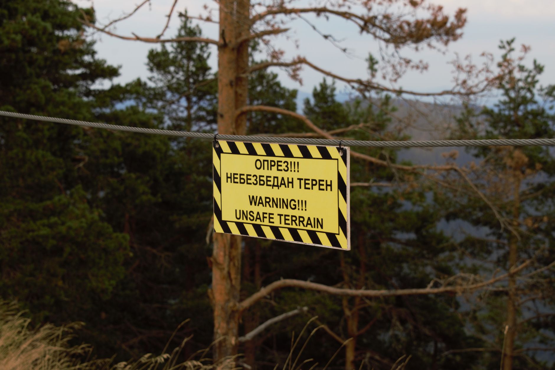 A warning sign cautions about unsafe terrain in a forested area, indicating potential danger.