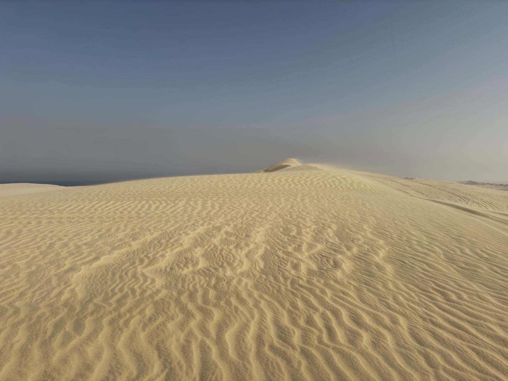 Serene desert landscape with golden sand dunes under clear blue sky at sunrise.