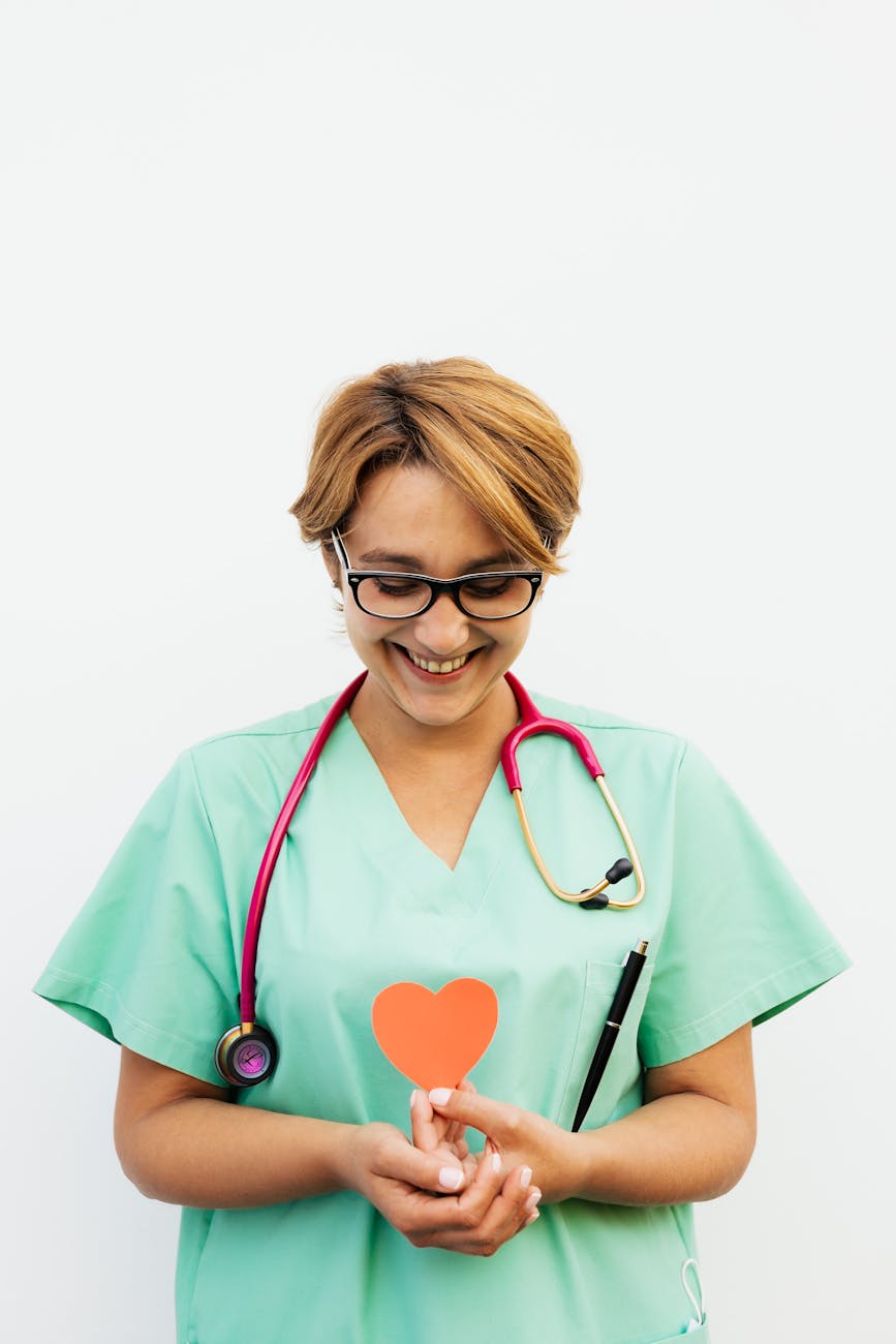 Smiling nurse in scrubs holding a paper heart symbol, promoting heart health awareness.