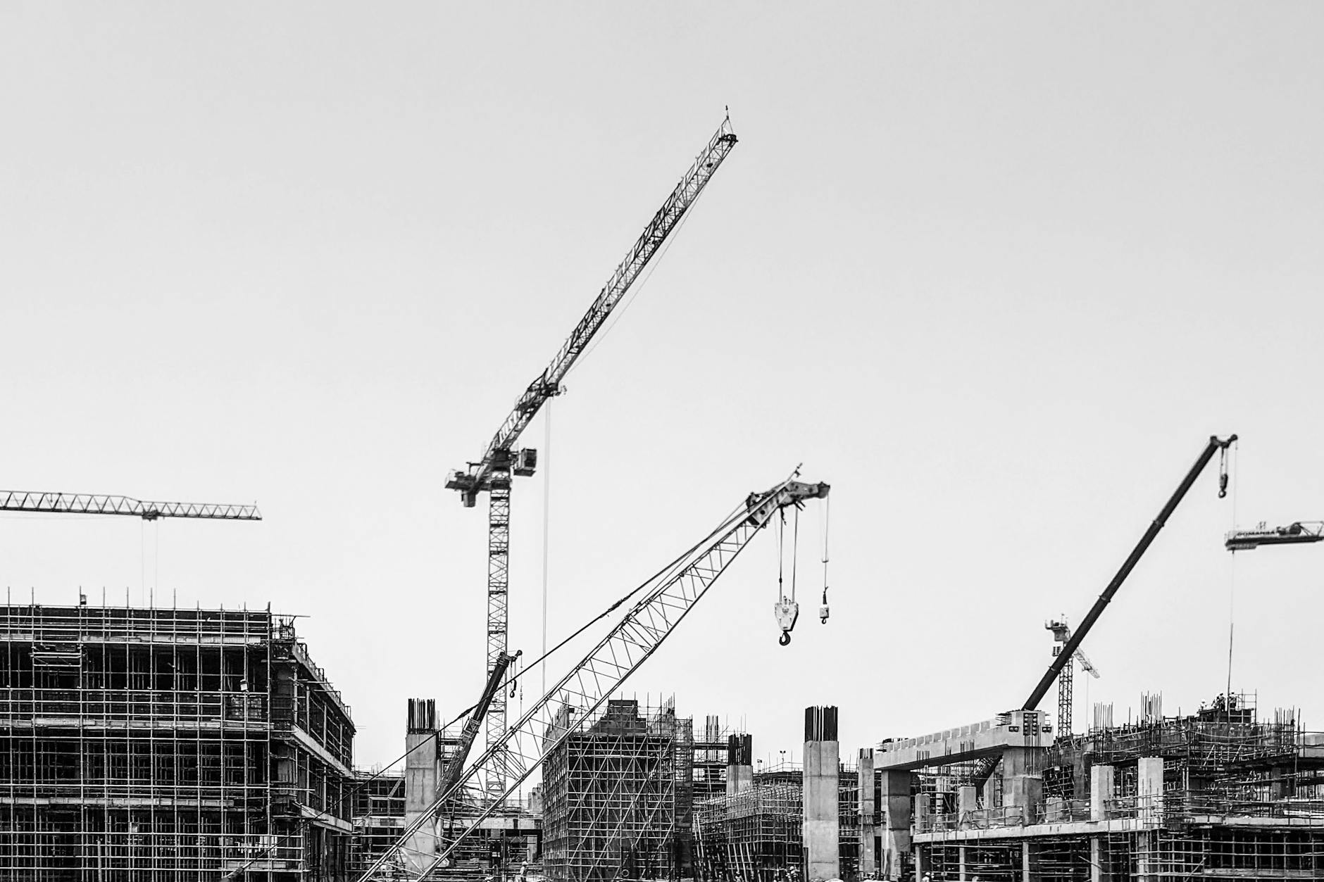 Black and white image of cranes working on a large construction site under a clear sky.