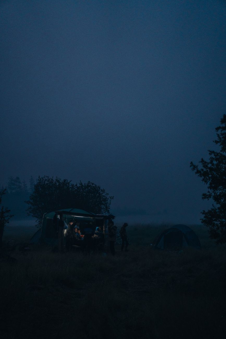 An atmospheric night camping scene with tents and silhouetted people surrounded by dense fog in Якутия, Россия.