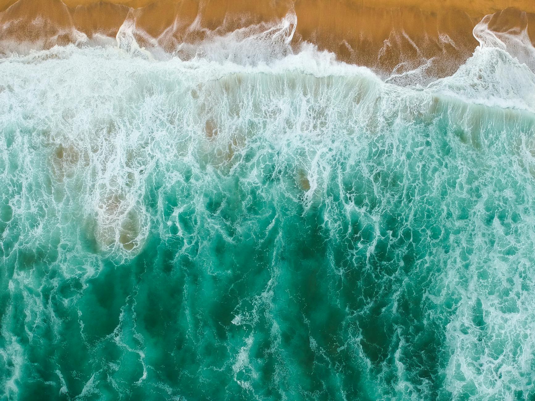 Stunning aerial shot of turquoise ocean waves meeting the sandy shore with foamy patterns.