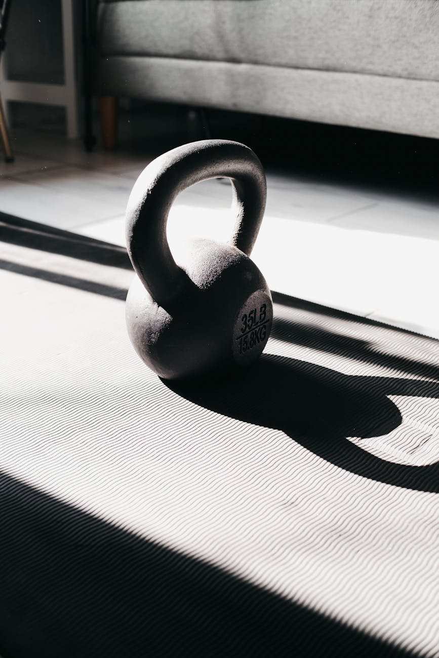 Kettlebell in bright sunlight casting shadow on gym mat indoors, perfect for fitness themes.