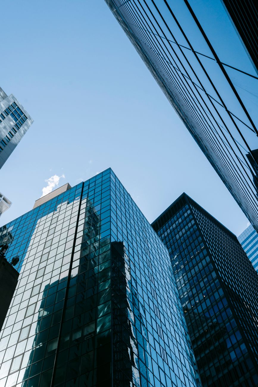 From below of glittering mirrored walls of contemporary high skyscrapers located against cloudless blue sky on sunny day