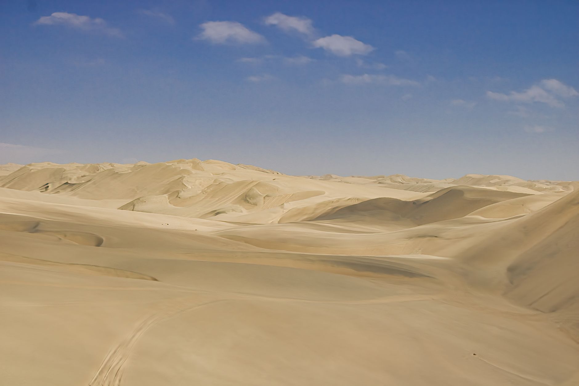 Serene aerial view of rolling sand dunes under a clear blue sky in the Namibian desert.