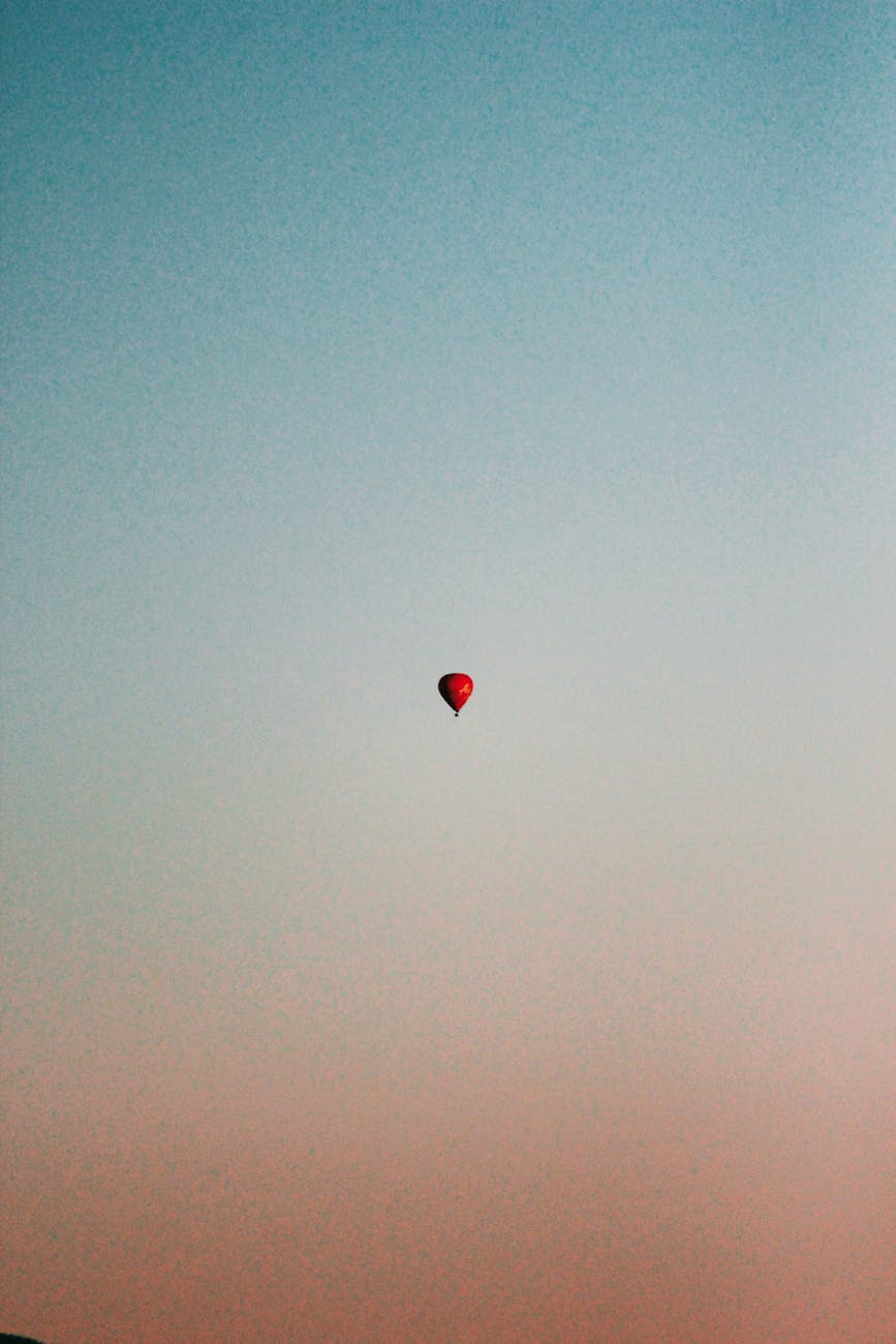 A solitary hot air balloon ascends in a tranquil sky at sunset, offering a serene and minimalistic view.