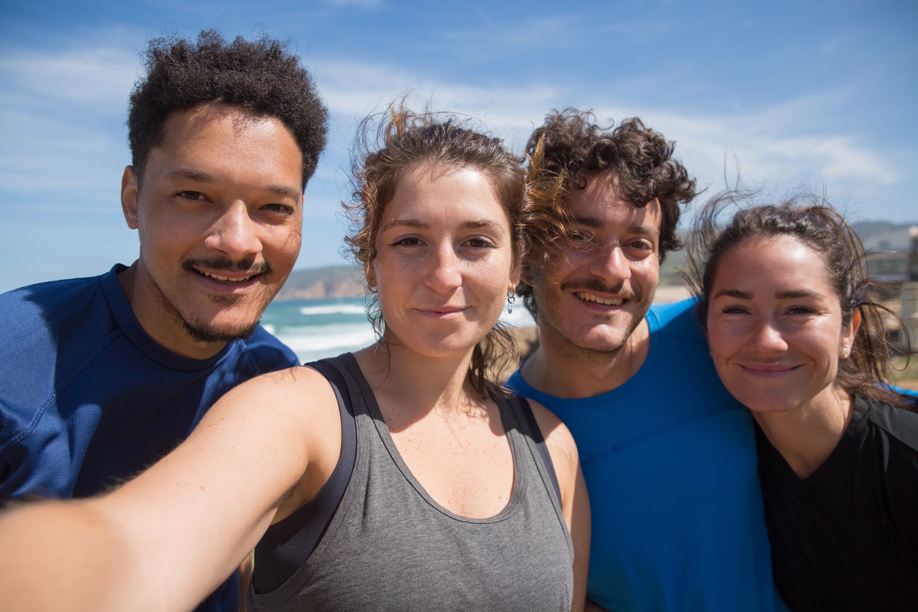 Four young adults smiling at the beach, capturing a joyful moment under the sunny sky.