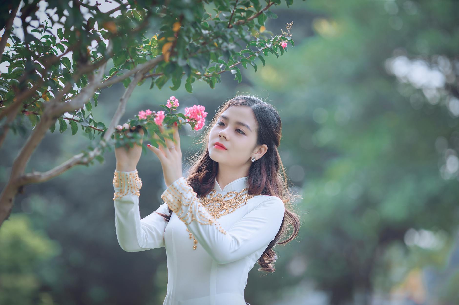 An elegant woman in traditional Ao Dai appreciating the beauty of pink blossoms.