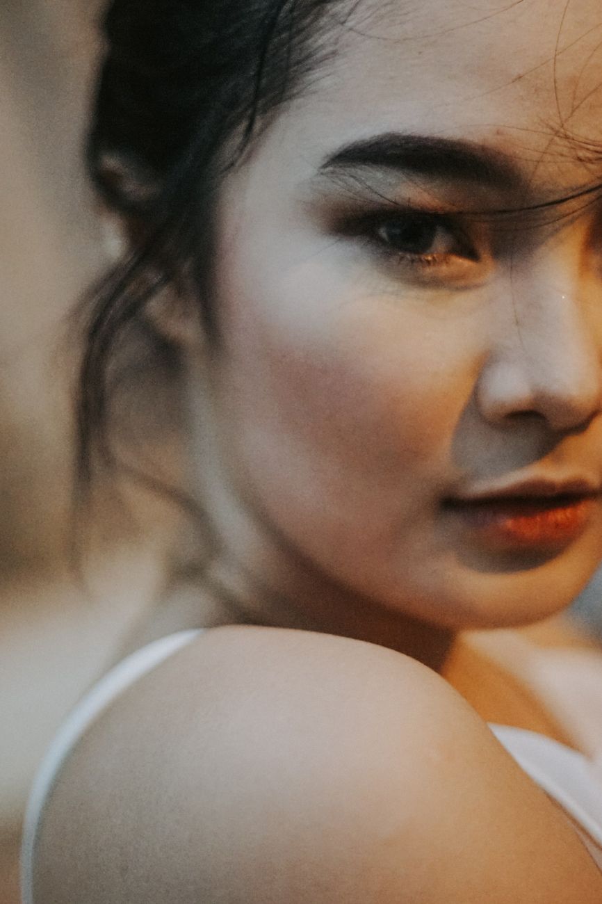 A captivating portrait of an Asian woman with a contemplative expression, in soft lighting.
