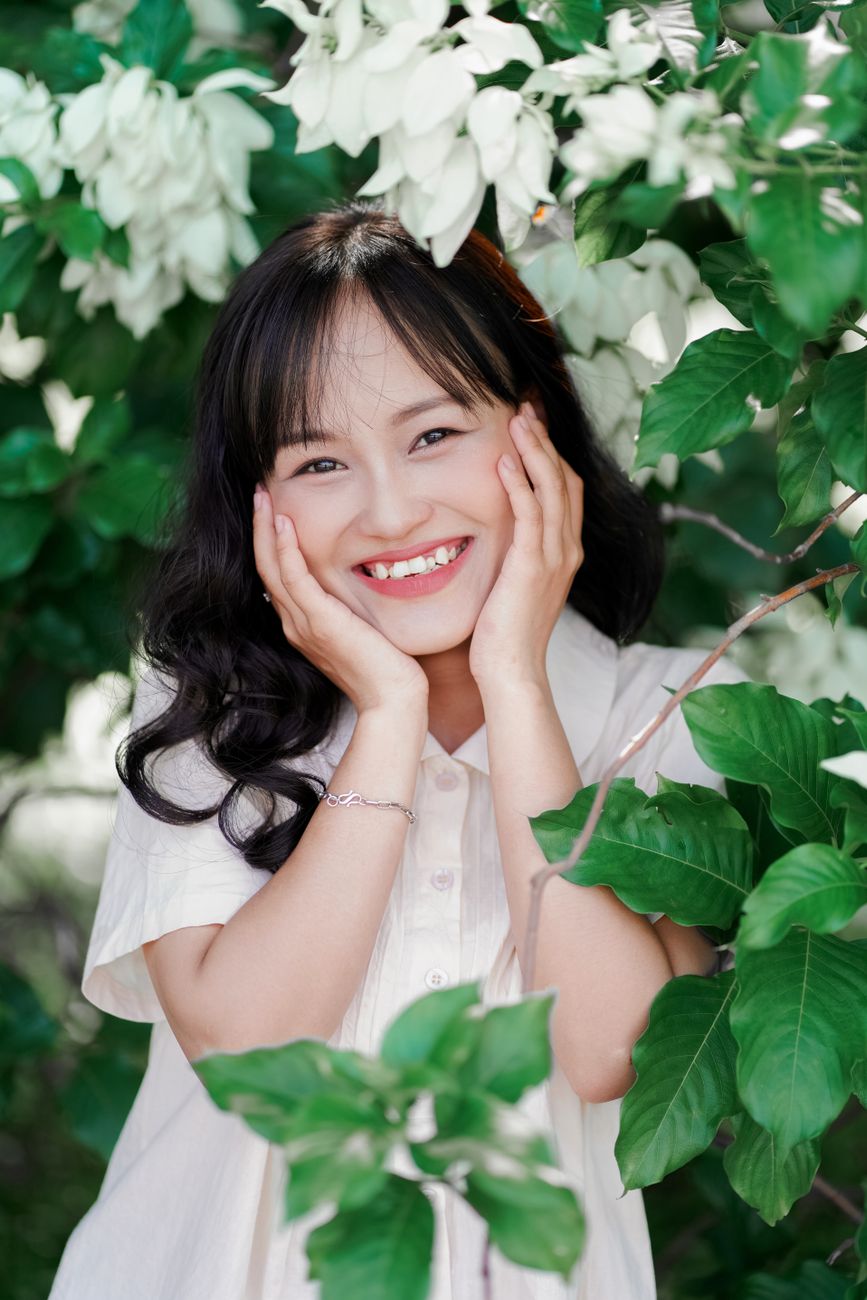 A smiling woman poses amid lush green foliage, exuding happiness and natural beauty.