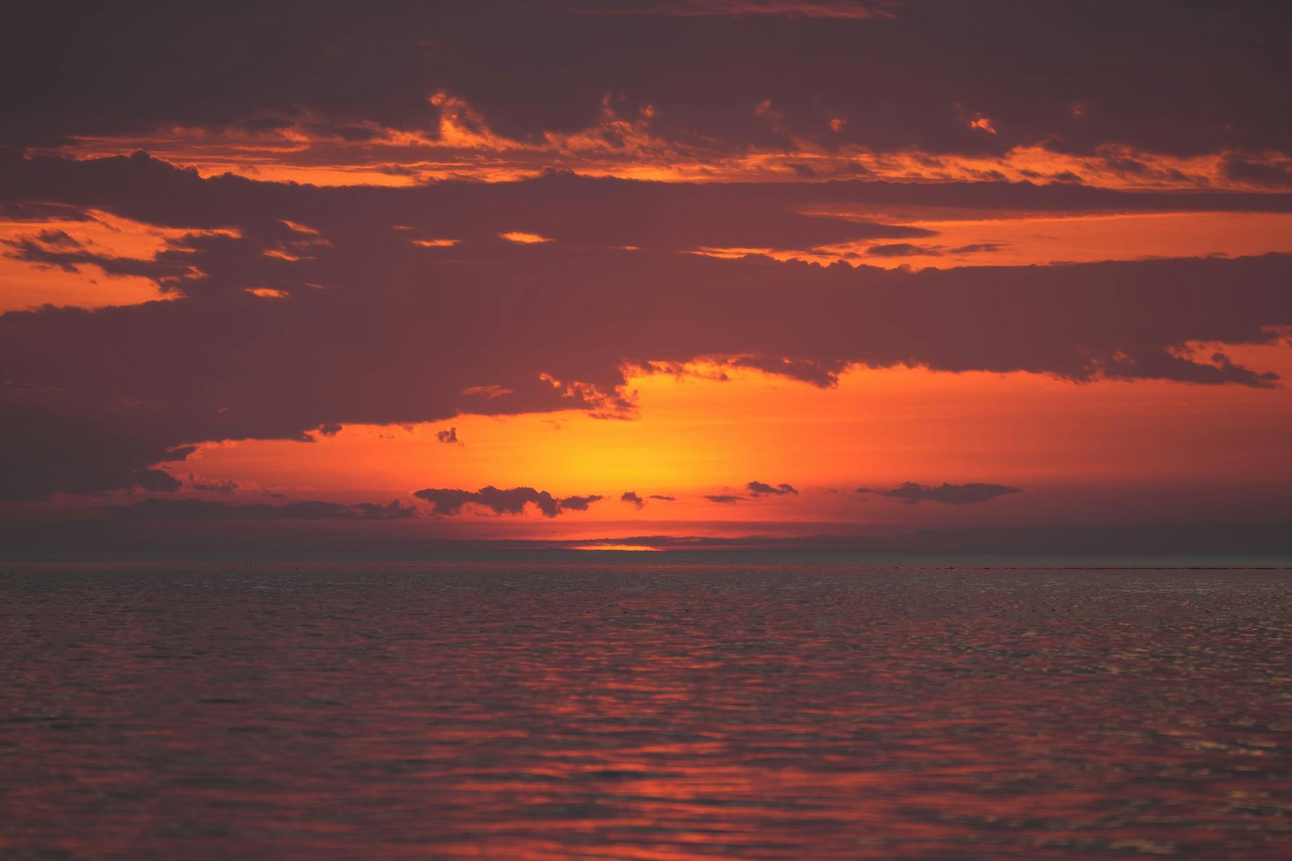 Vivid sunset over tranquil ocean waters, featuring dramatic clouds and rich orange hues.