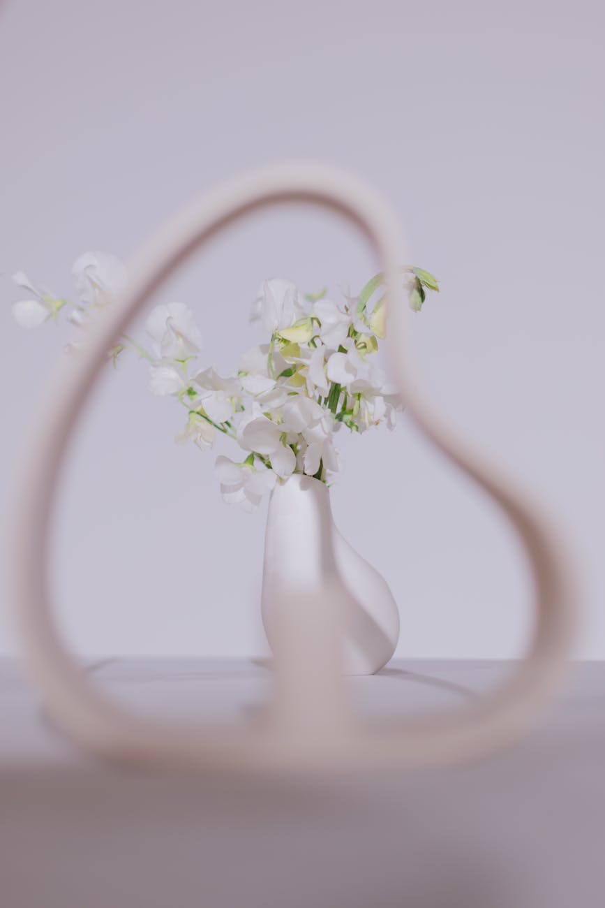 Artistic photo of a minimalist ceramic vase with white flowers framed by abstract shape.