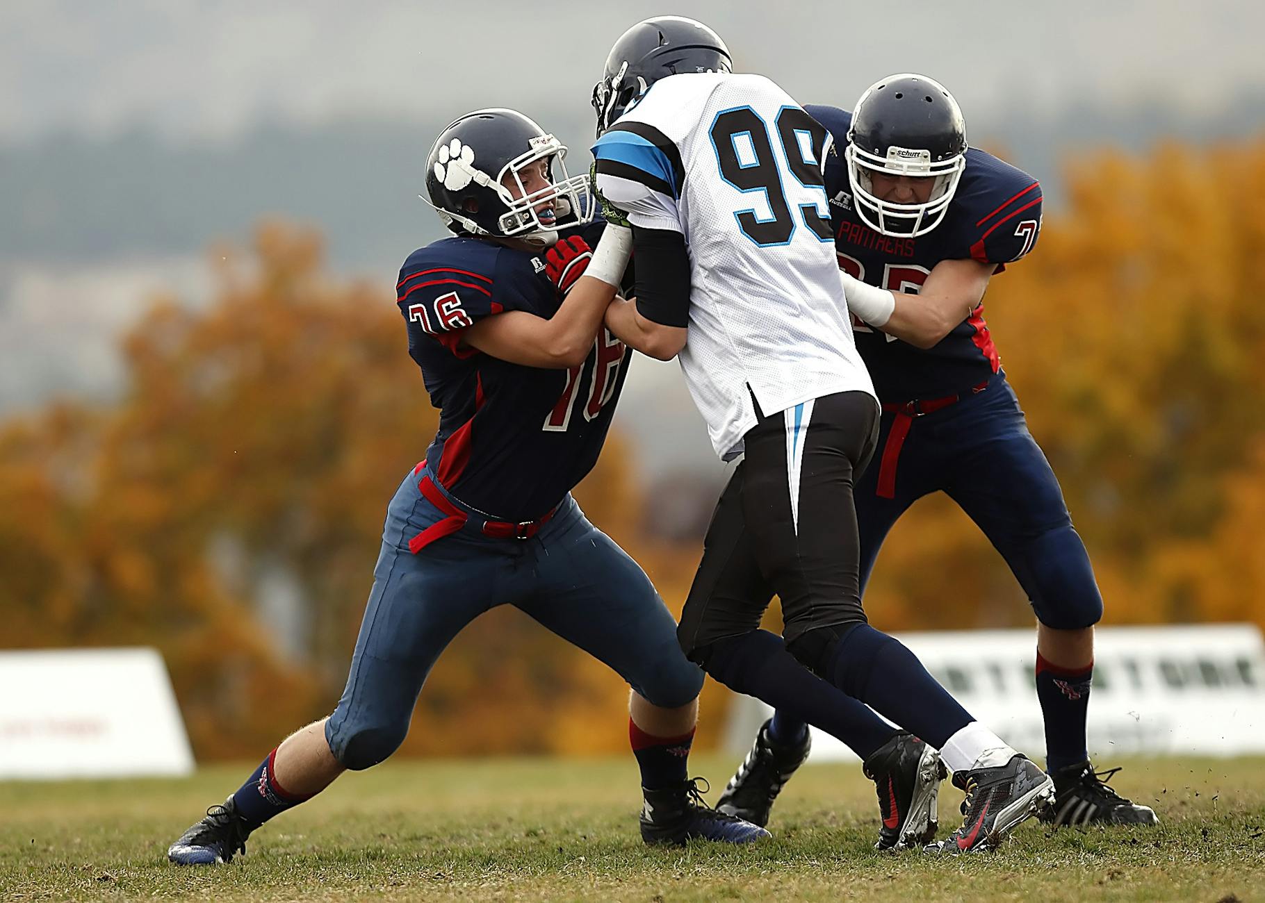 Football players in action during a competitive game on a field with autumn foliage.