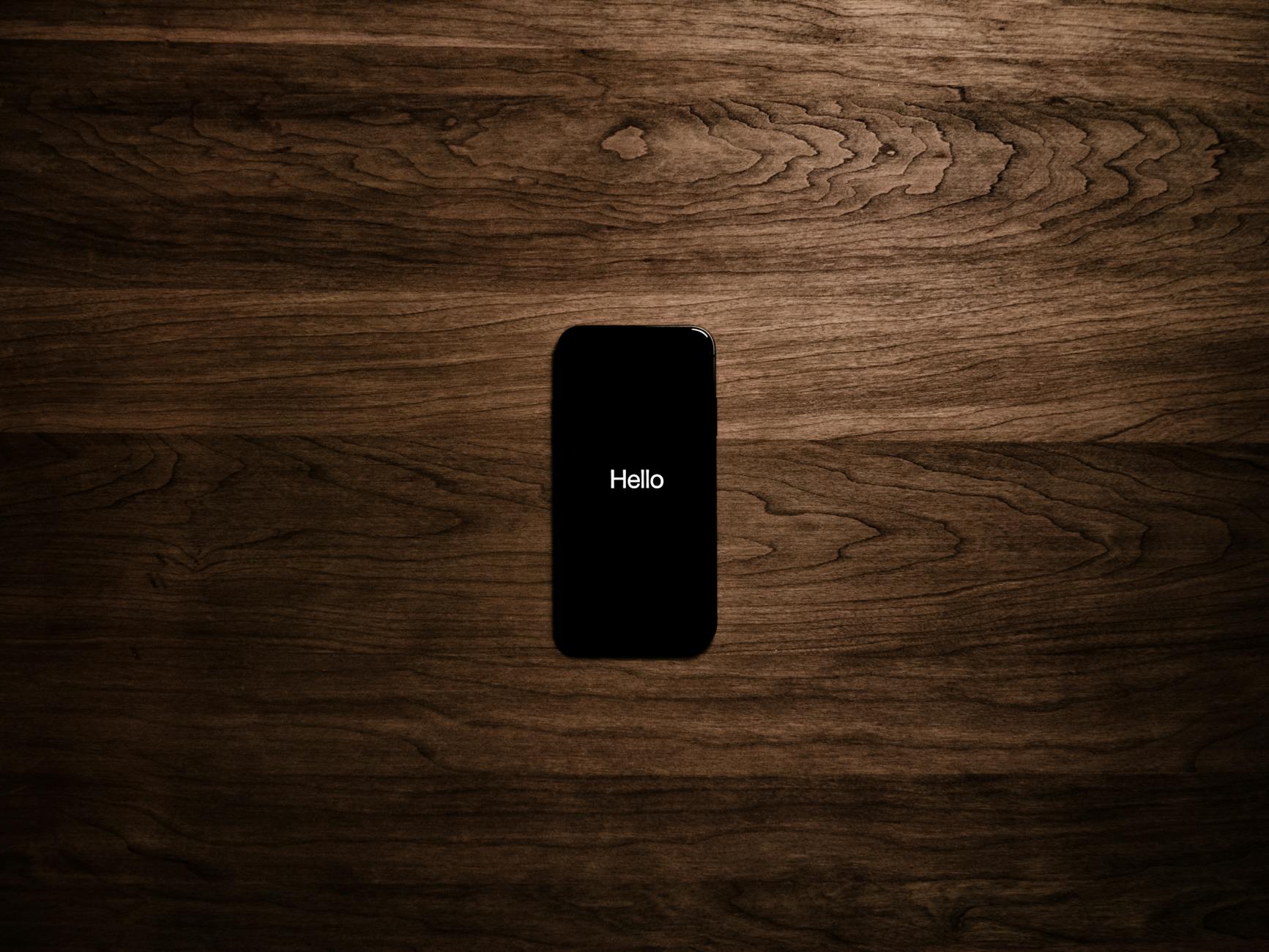 A smartphone displays 'Hello' against a dark wooden background, offering a sleek tech aesthetic.