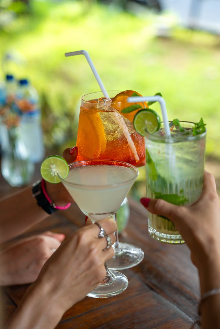 Three hands toasting with vibrant cocktails in an outdoor setting, perfect for summer gatherings.