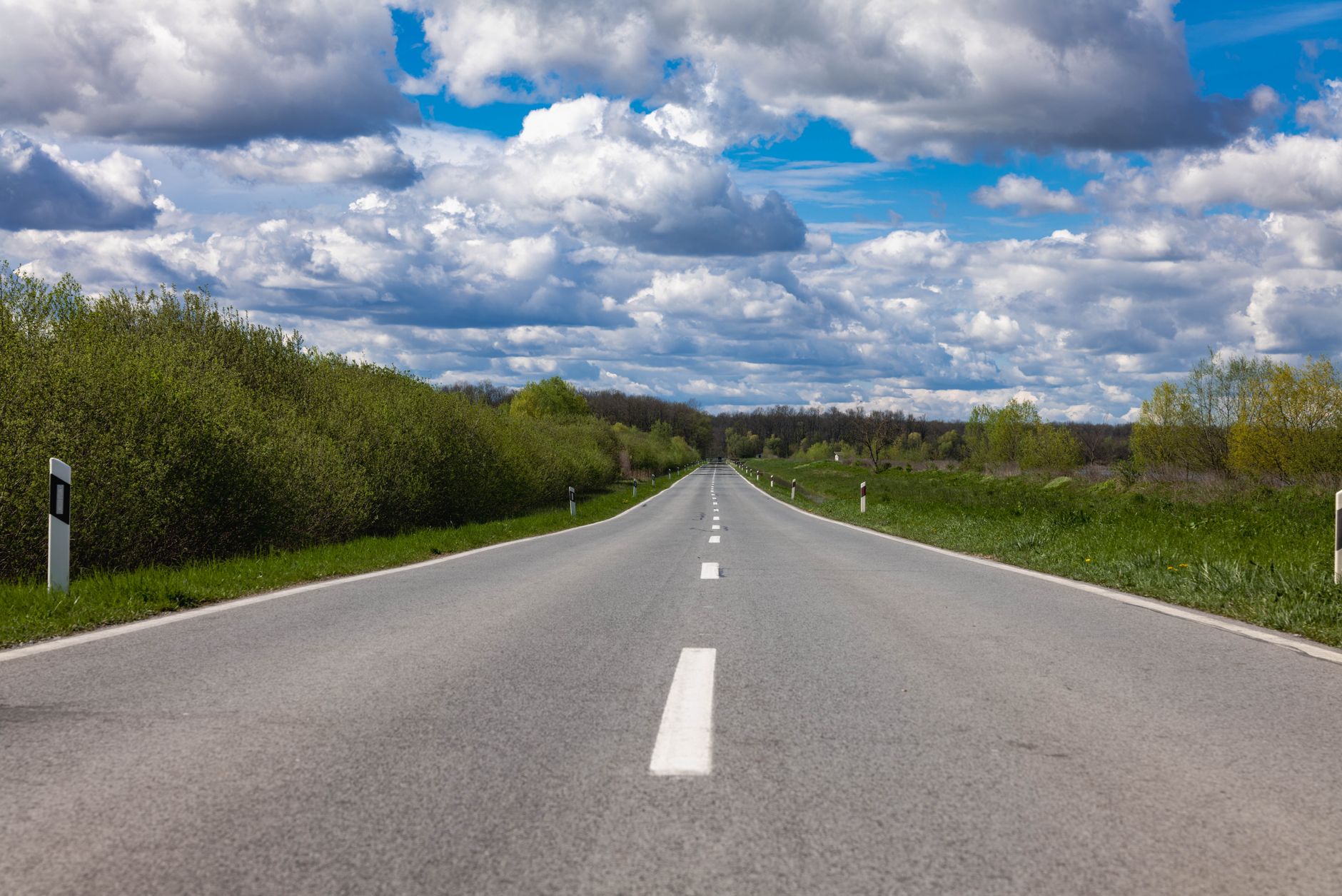 Open countryside road stretching into the horizon under a sky filled with dramatic clouds.