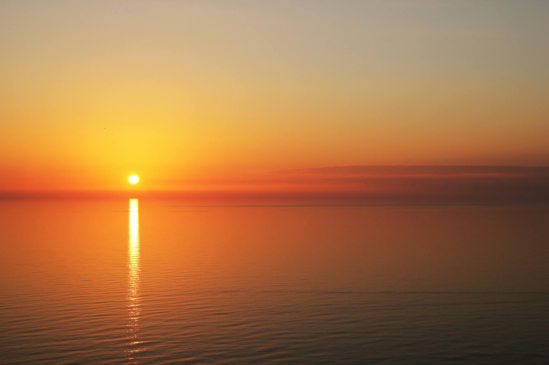 A tranquil sunset over calm ocean waters with golden reflections in the sky and sea.