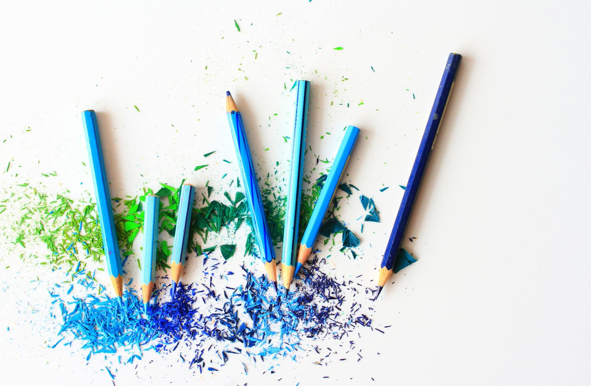 Creative display of colored pencils and vibrant shavings on a white background.