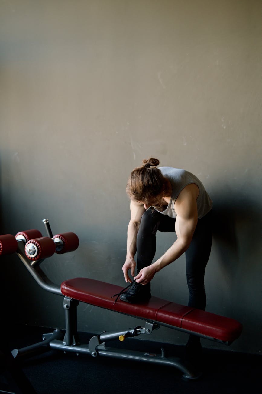 Muscular man preparing for workout, tying shoes in a modern gym environment.