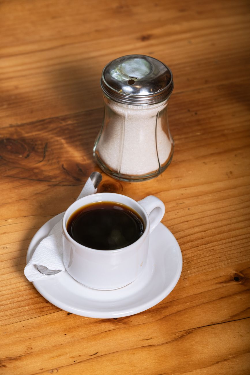 A warm cup of black coffee with sugar jar on a rustic wooden table, evoking a cozy morning vibe.