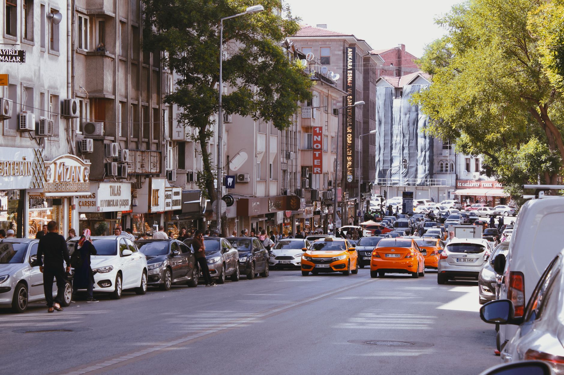 Vibrant city street scene featuring taxis, parked cars, and pedestrians on a sunny day.