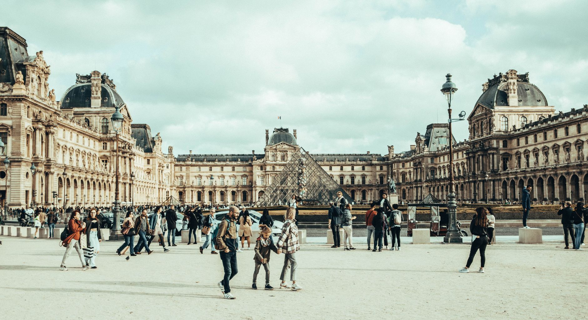 A bustling scene of people walking in front of the iconic Louvre Museum, Paris.