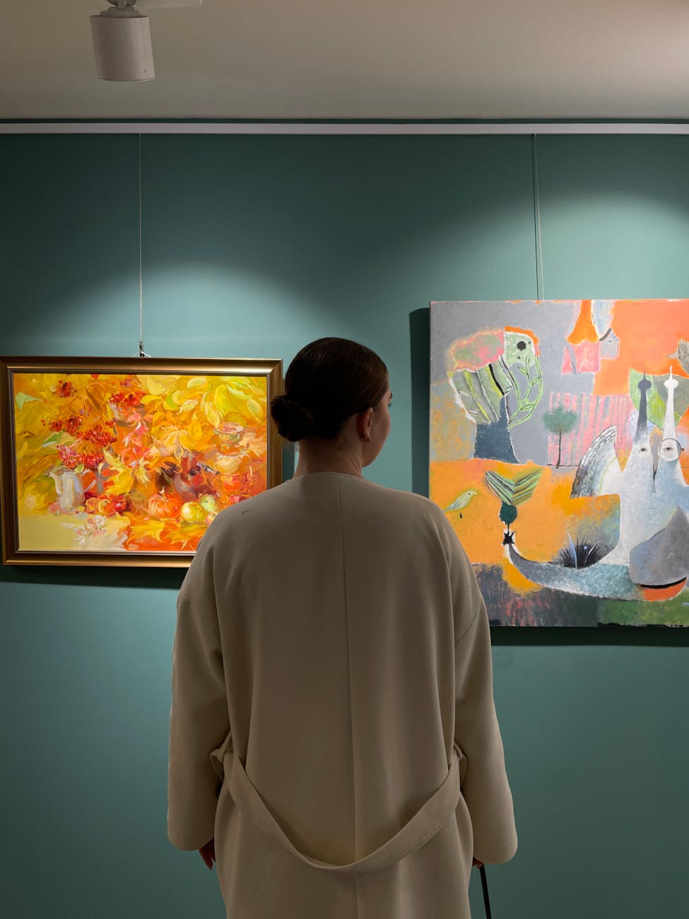 A woman in a gallery observing colorful abstract art on a blue wall.