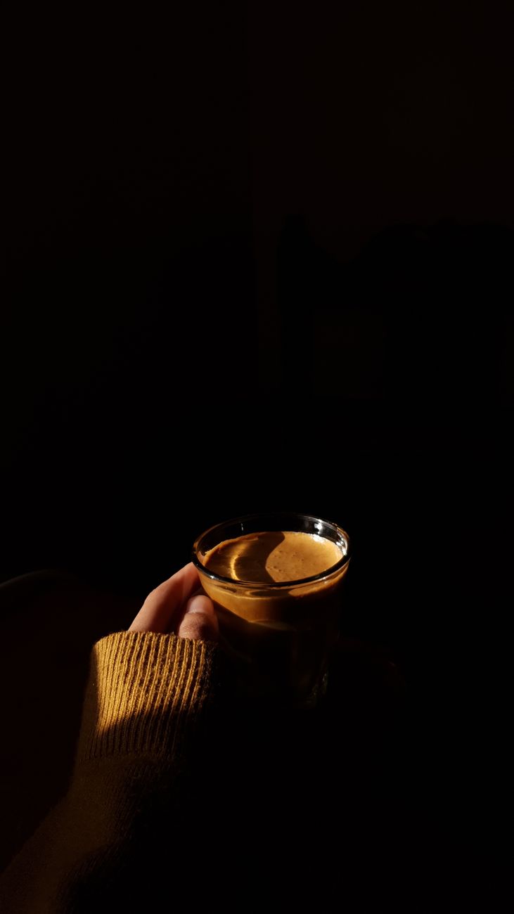 A person holds a warm drink in a dimly lit room, creating a cozy ambiance.